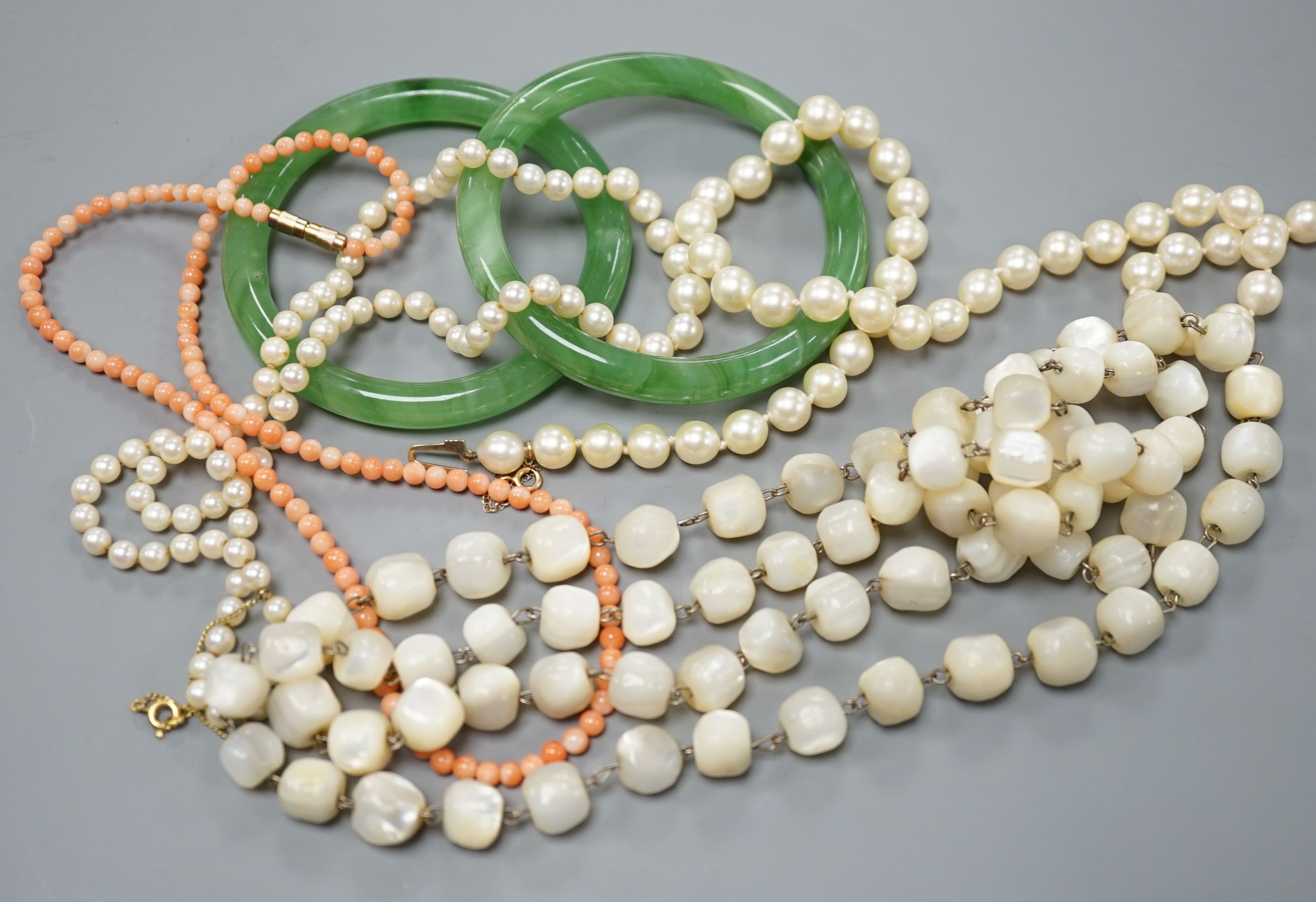 Two single strand cultured pearl necklaces, one with 9ct gold clasp, two green glass bangles, a coral bead necklace and a mother of pearl bead necklace.